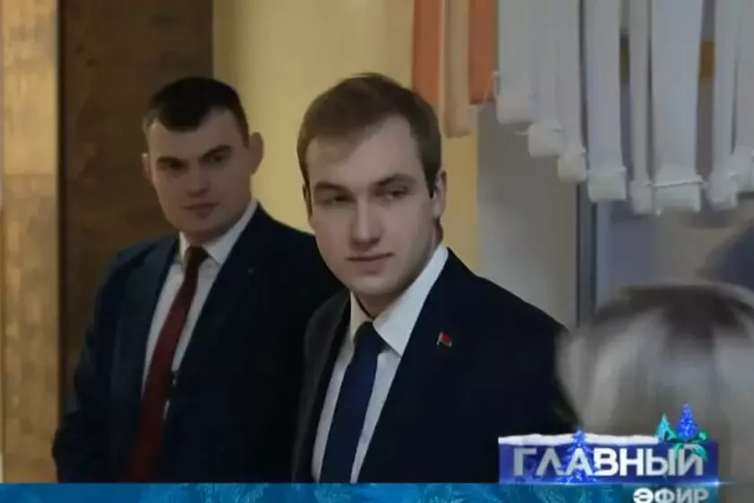 Artiem Sobieŝanskij stoit za śpinoj Nikołaja Łukašienko vo vriemia intierv́ju. Minsk, 5 janvaria 2025 hoda. Skrinšot: NEWS.BY: novosti Biełarusi i mira, YouTube